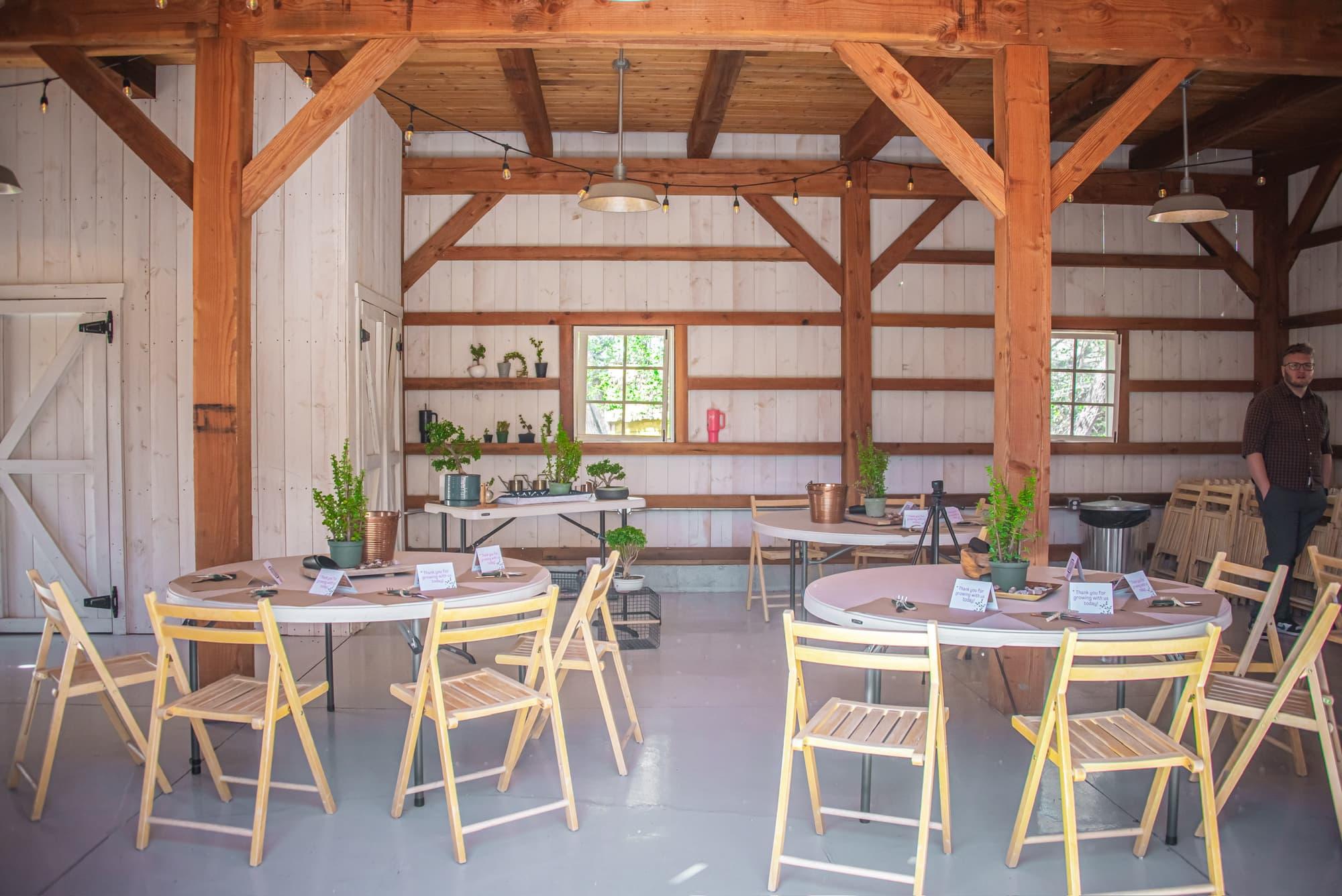 Wood-beamed barn with round tables and folding chairs set for a workshop, dwarf jade plants on shelves